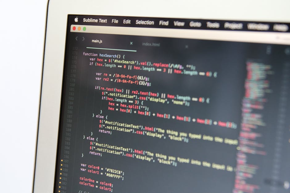 A close-up of a computer screen displaying lines of colorful code on a dark background, with text in shades of red, green, blue, and white. The screen appears to be part of a laptop or desktop monitor